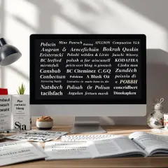 Na biurku stoi komputer z tekstem, gdzie widać polskie znaki. Obok kubek, książki i lampka.