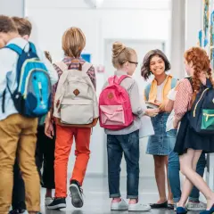 Uczennica i jej koledzy rozmawiają w szkolnym korytarzu, każdy z plecakiem gotowym na nowy dzień nauki.