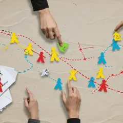 Ręce układają kolorowe papierowe ludziki, tworząc ścieżki. To jak gra, w której dzieci uczą się współpracy i planowania.
