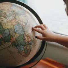 Dłoń dziecka wskazuje na globus, być może planując podróż lub badając historię **diaspory**.