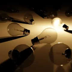 Rozproszone żarówki, jedna świeci, tworząc grę światła i cienia. Fenomenologia idei w mroku.