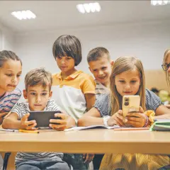 Dzieci skupione na ekranach telefonów i tabletu, uczące się i bawiące razem. Wspólna **socjalizacja** w cyfrowym świecie.