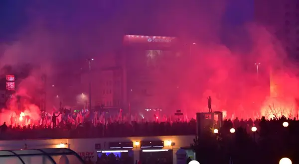 Tłum z polskimi flagami, race i dym tworzą atmosferę manifestacji. W tle widać budynki i billboard Santander. To obraz silnego nacjonalizmu.