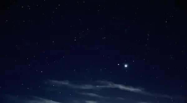 Nocne niebo pełne gwiazd, z widocznymi chmurami i dwoma jasnymi punktami, być może planetami.