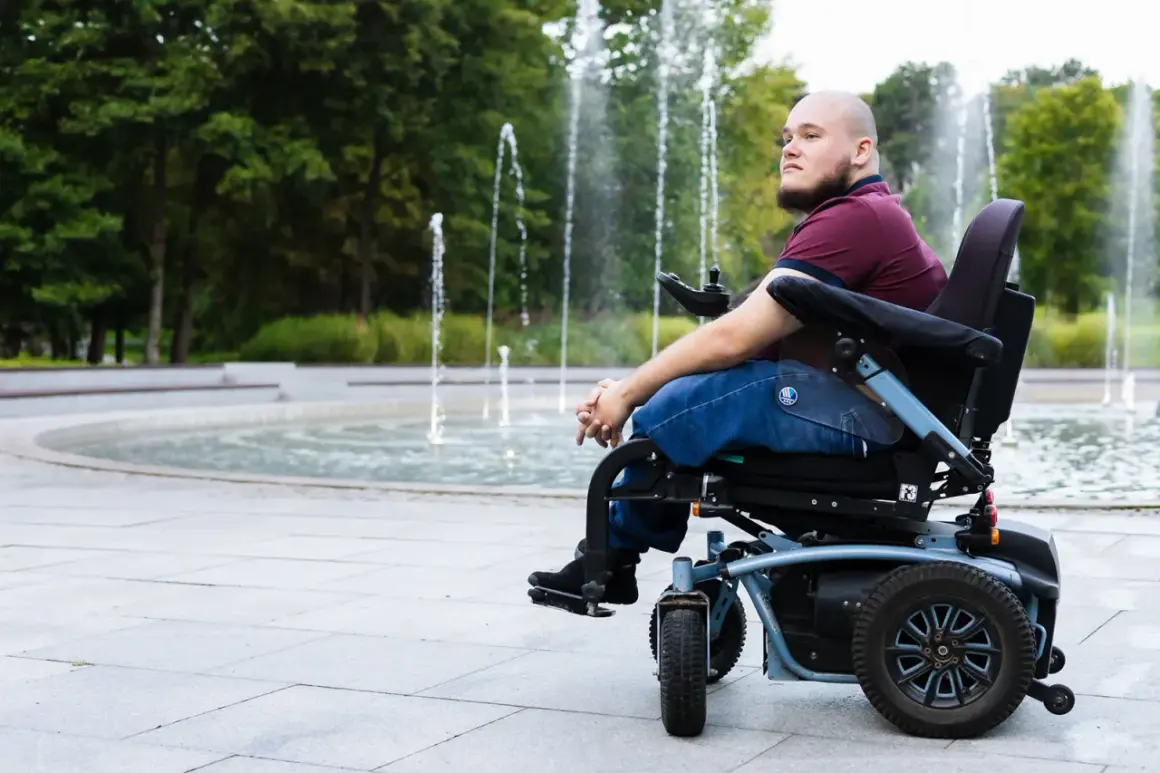 Mężczyzna na wózku inwalidzkim patrzy w dal, siedząc przy fontannie.