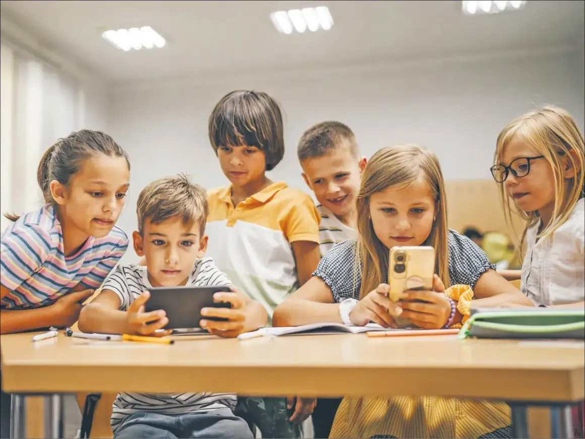 Dzieci skupione na ekranach telefonów i tabletu, uczące się i bawiące razem. Wspólna **socjalizacja** w cyfrowym świecie.